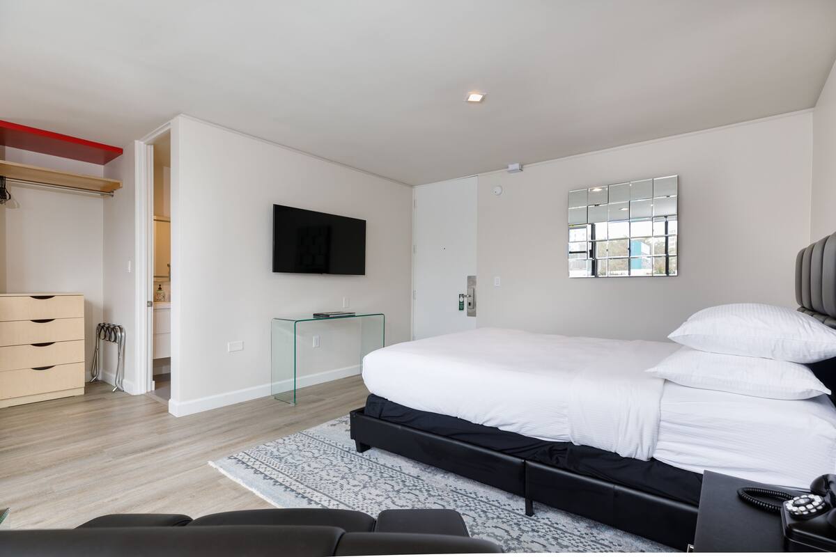 A modern bedroom with a large bed, a bedside table, a TV mounted on the wall, and a mirror.