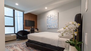 Een moderne slaapkamer met een groot bed, een flatscreen televisie, een potorkidee en een kamerbreed tapijt met dessin.
