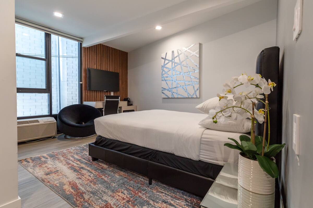 A modern bedroom with a large bed, a flat-screen TV, a potted orchid, and a patterned rug.
