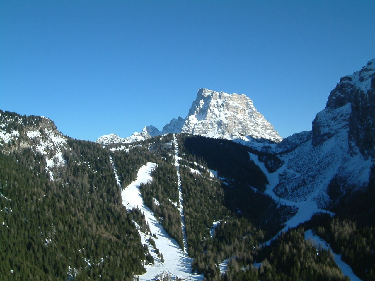 A mountainous landscape with snow-covered peaks and dense forest.