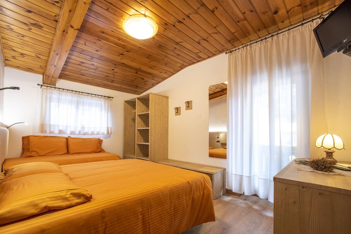 A bedroom with a wooden ceiling, a bed with a headboard, a bedside table, a mirror, and a lamp.