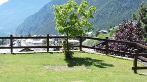 A grassy area with a wooden fence, a small tree, and a mountain backdrop. - Hotel Maisonnette (Torgnon)