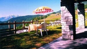 An outdoor seating area with a table and chairs, a stone pillar, and a view of mountains. - Hotel Maisonnette (Torgnon)