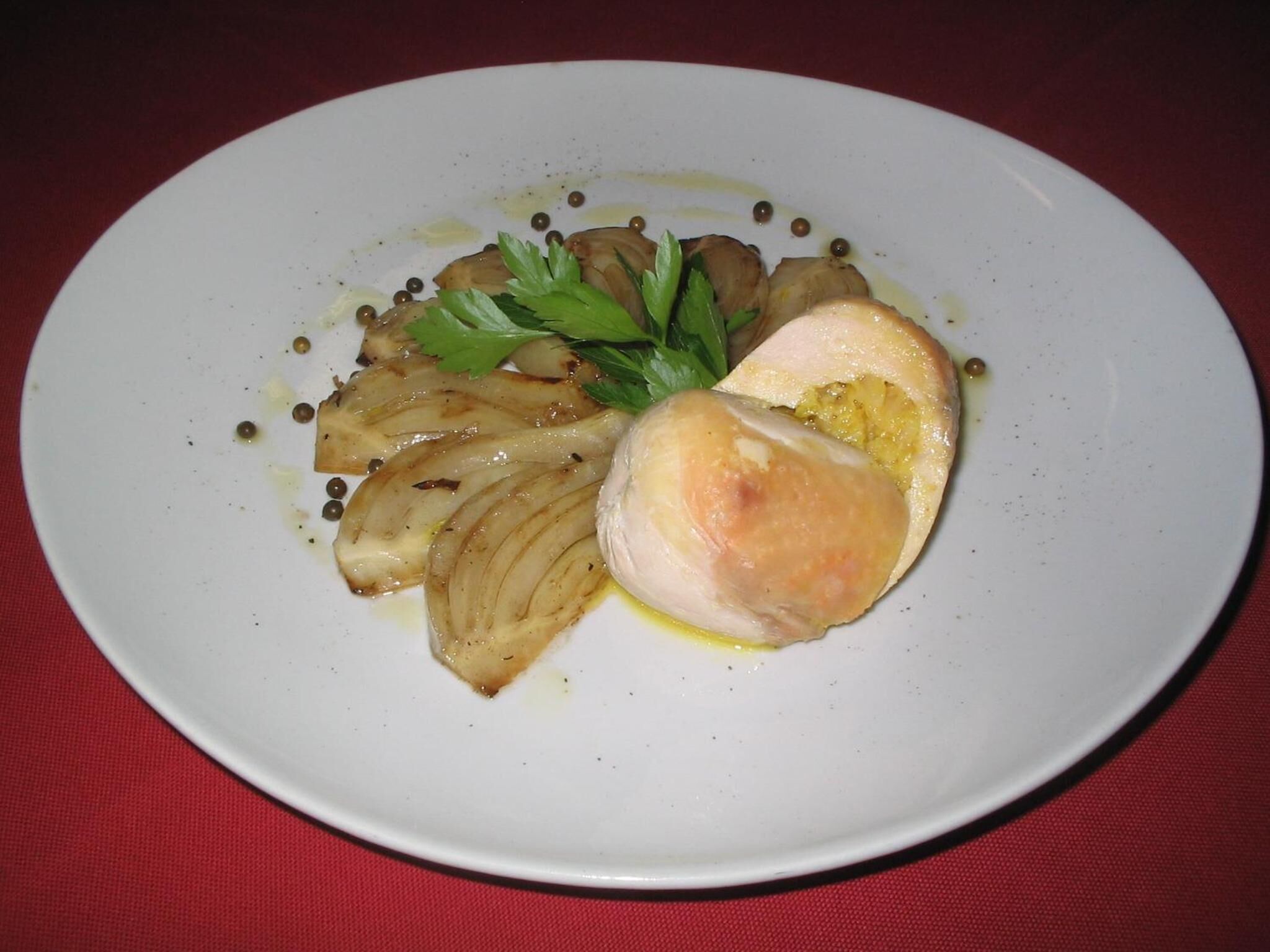 A white plate with sliced onions, a piece of chicken, and a garnish on a red tablecloth.