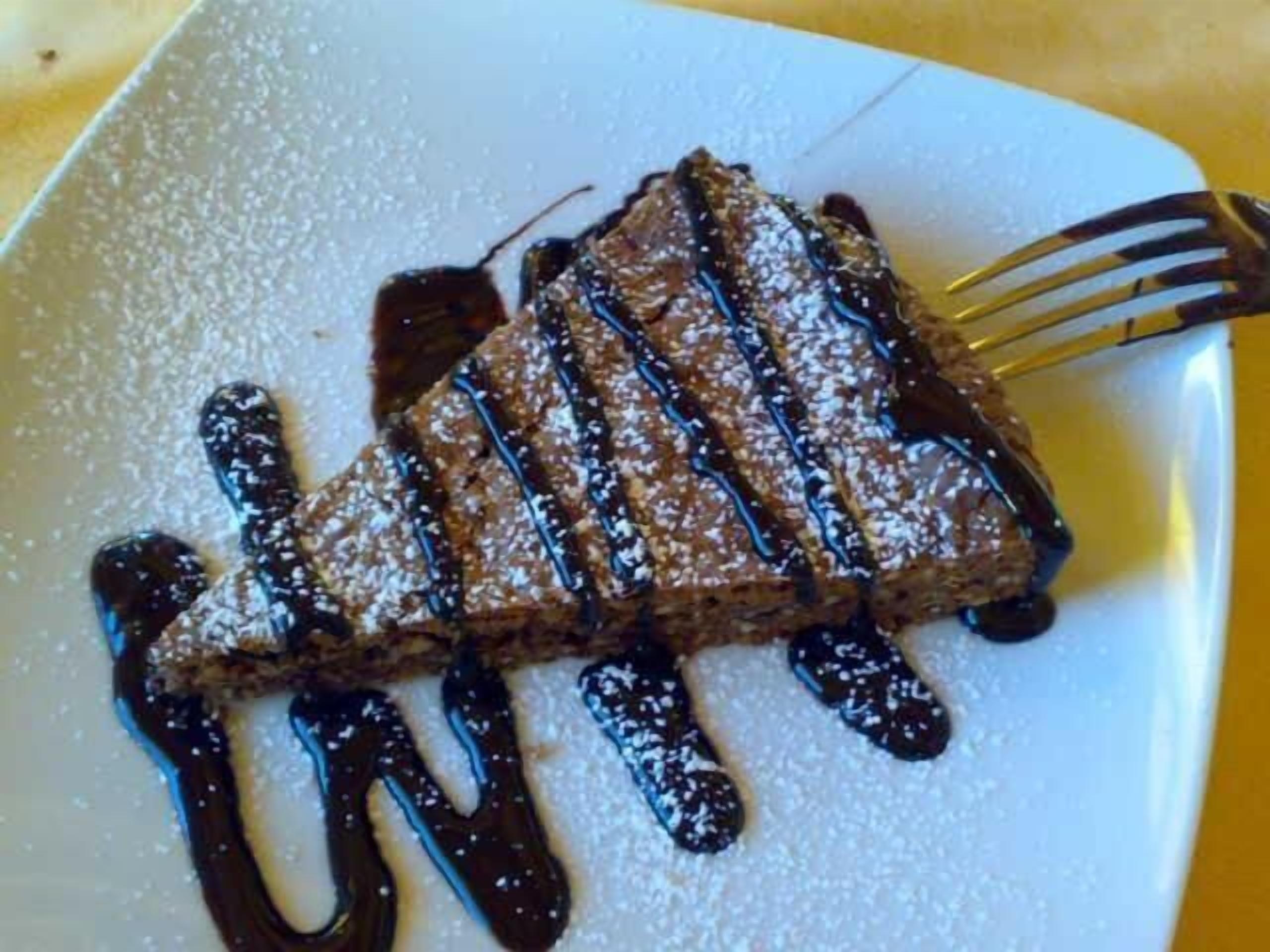Un dessert servi dans une assiette blanche, nappé de chocolat fondu et saupoudré de sucre glace.
