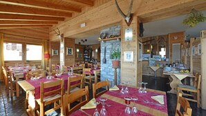 A wooden interior with tables set for dining, a stone fireplace, and wooden beams on the ceiling. - Hotel Maisonnette (Torgnon)