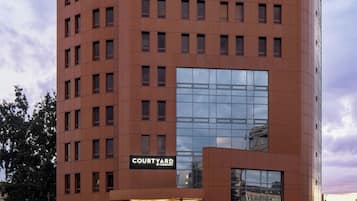 Um hotel com vários andares, fachada em vidro destacada e placa com a inscrição 'COURTYARD BY MARRIOTT'.