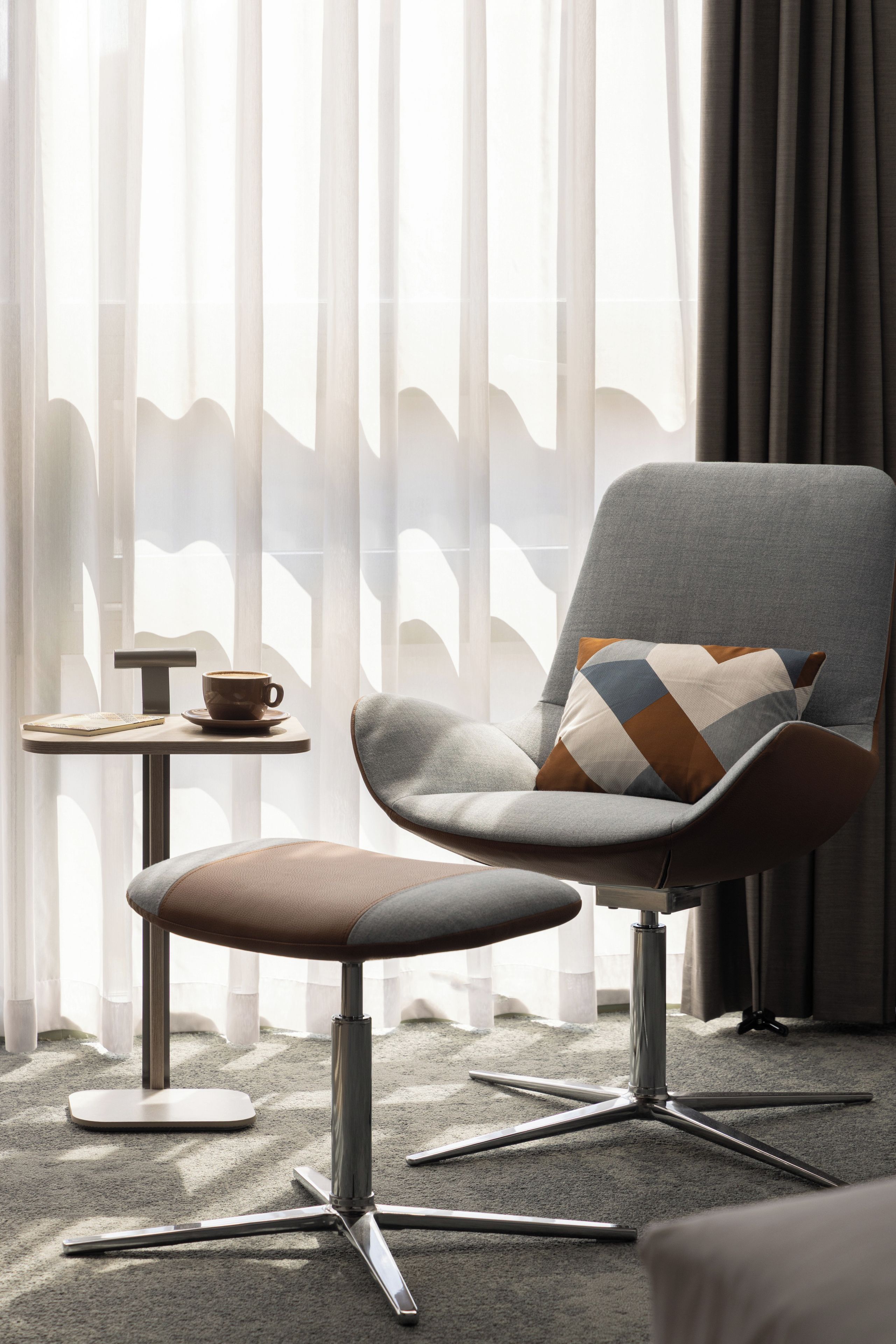 Een moderne fauteuil met een bekleed zitvlak en rugleuning, een metalen onderstel en een decoratief kussen.