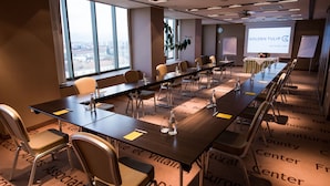 A conference room with a long table, chairs, a projector screen, and a large window. - Courtyard by Marriott Downtown Sibiu (Sibiu)
