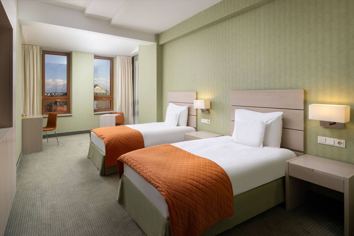 Une chambre d’hôtel avec deux lits, un bureau, une chaise et une fenêtre avec des rideaux.