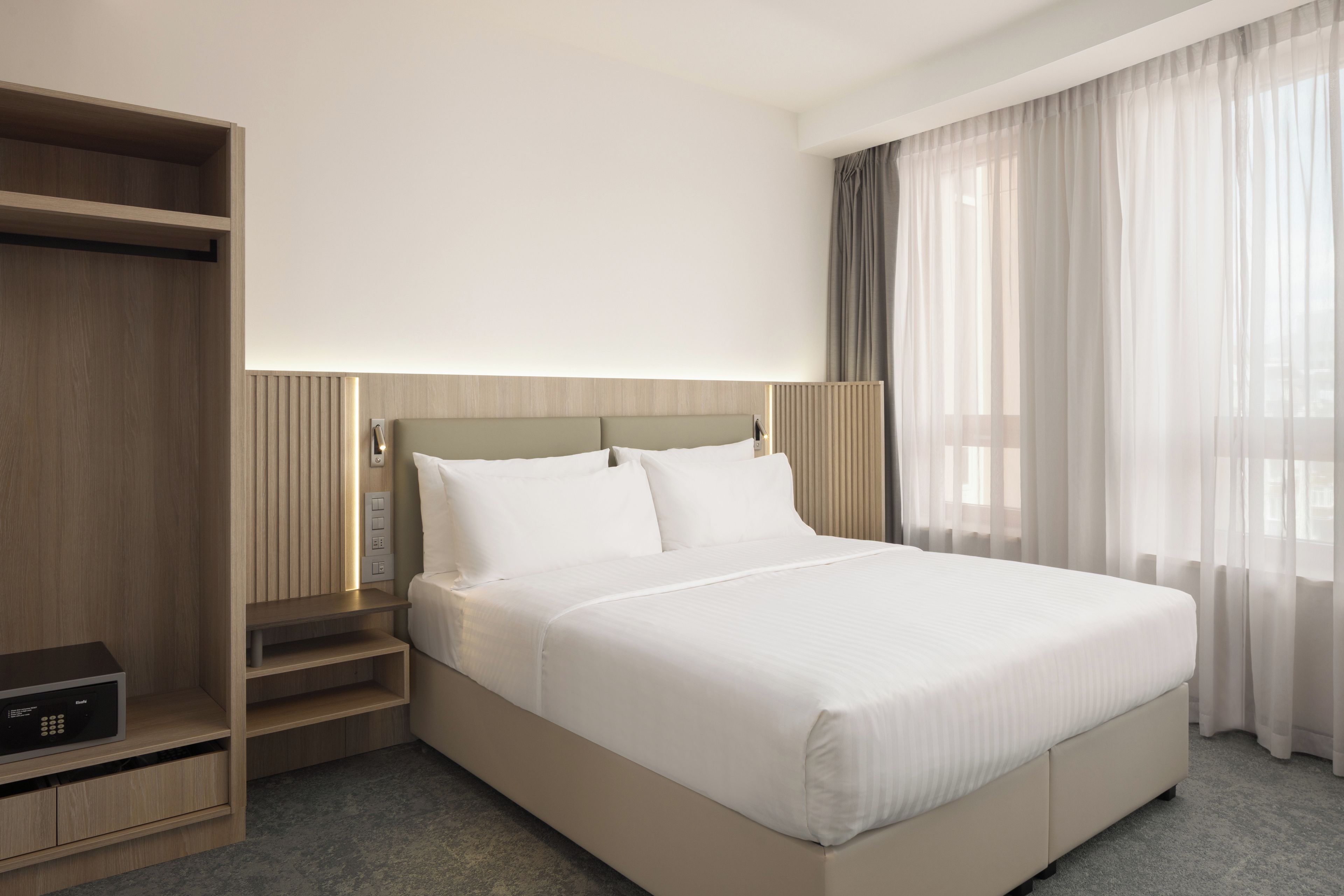 A hotel room with a bed, a wardrobe, a bedside table, and a window with curtains.