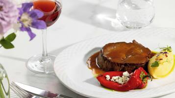 Un plato de comida con un filete, un pimiento rojo y un vegetal amarillo, acompañado de una copa de vino tinto.