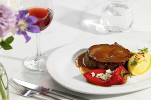 Un plato de comida con un filete, un pimiento rojo y un vegetal amarillo, acompañado de una copa de vino tinto.