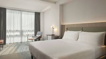 A hotel room with a large bed, a chair, a small table, and a lamp.