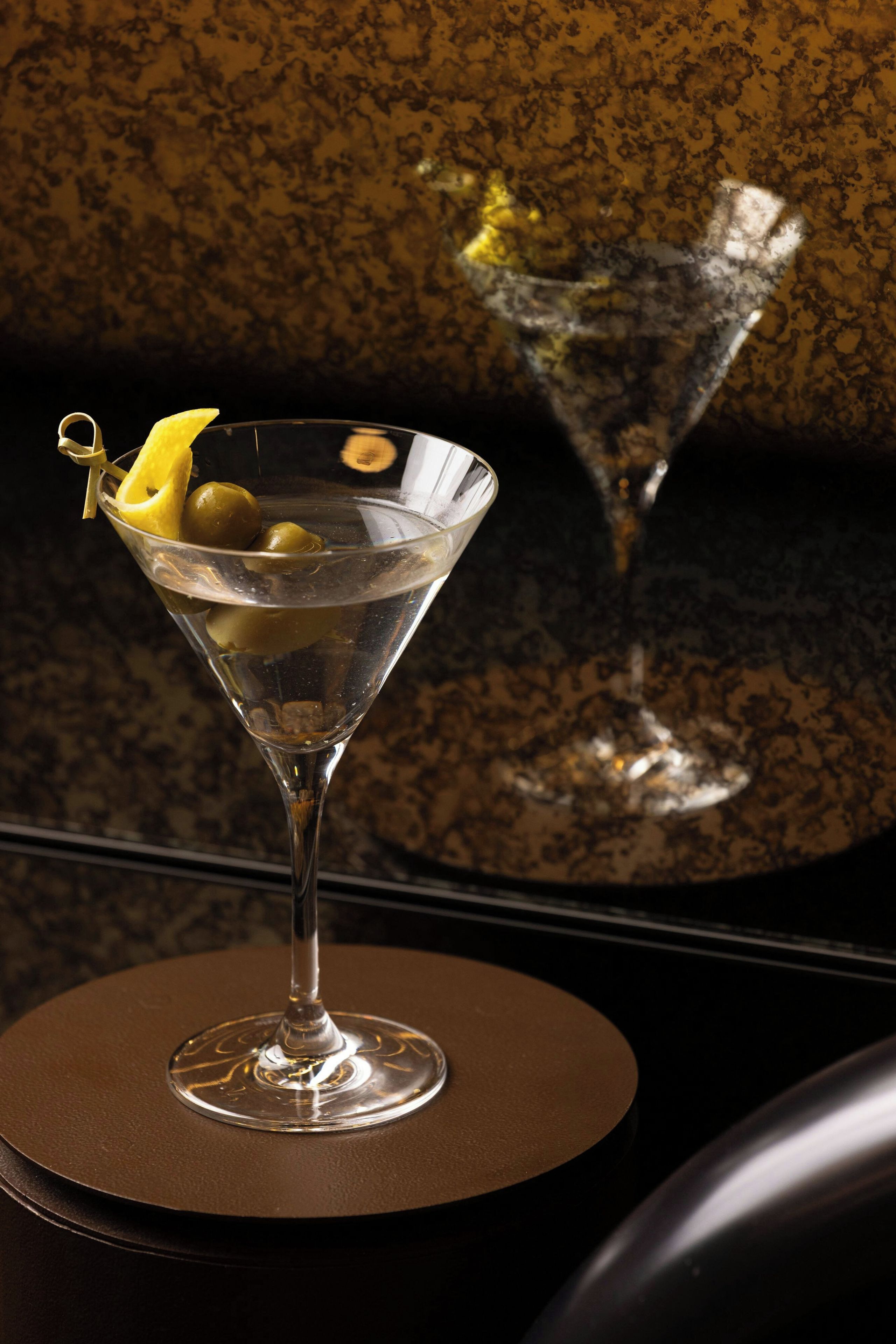 A martini glass with a lemon twist garnish on a round table.