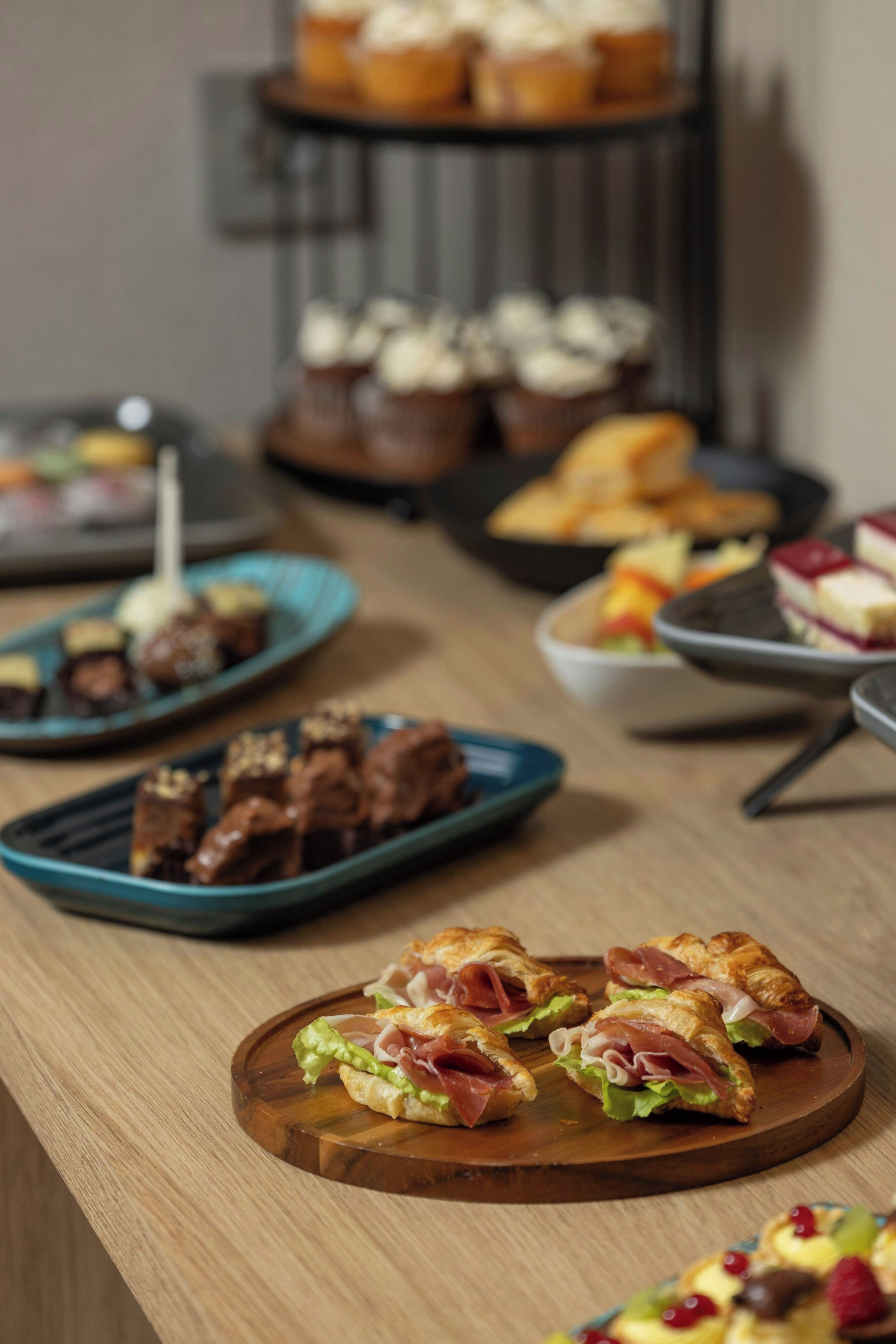 A variety of food items on a wooden table, including sandwiches and pastries.