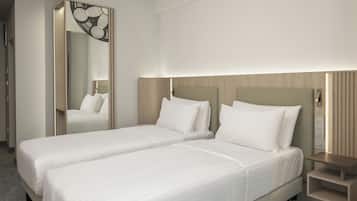 A hotel room with two single beds, a mirror, a bedside table, and a wall-mounted light.