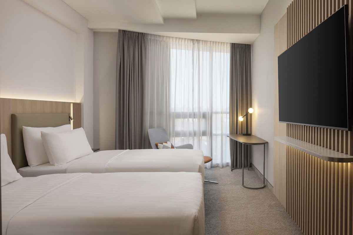 Een hotelkamer met twee bedden, een aan de muur bevestigde televisie, een bureau en een stoel.