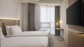 Habitación de hotel con dos camas, un televisor montado en la pared, un escritorio y una silla.