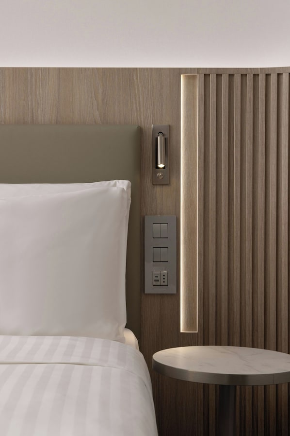 Habitación de hotel con cama, mesita de noche, panel de control en la pared y un panel vertical con luz.