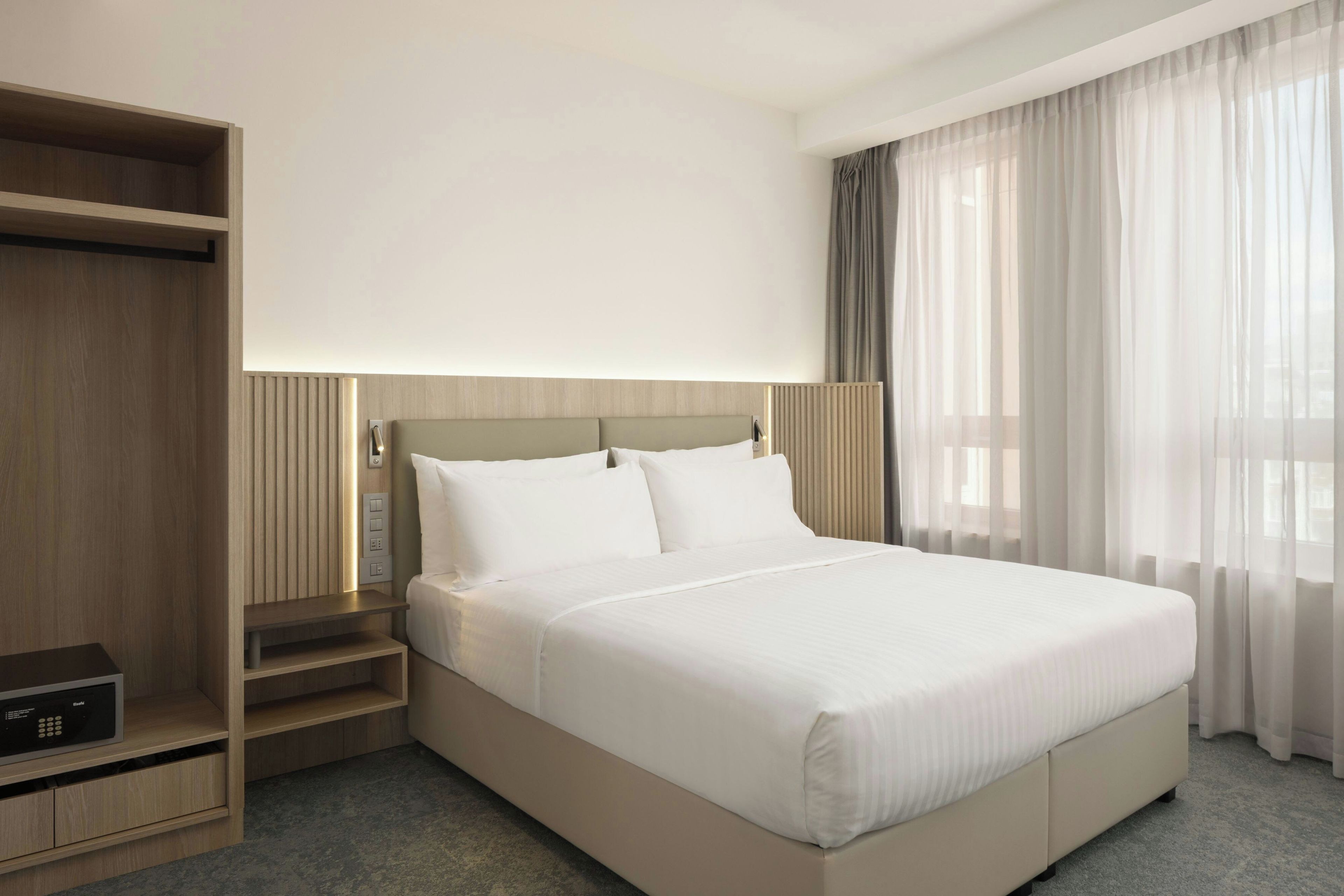 A hotel room with a large bed, a wardrobe, and a bedside table.