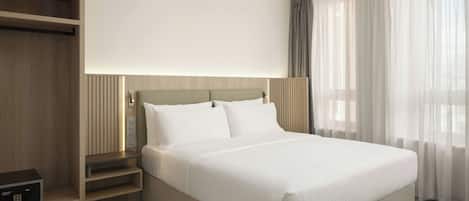 A hotel room with a large bed, a wardrobe, and a bedside table.