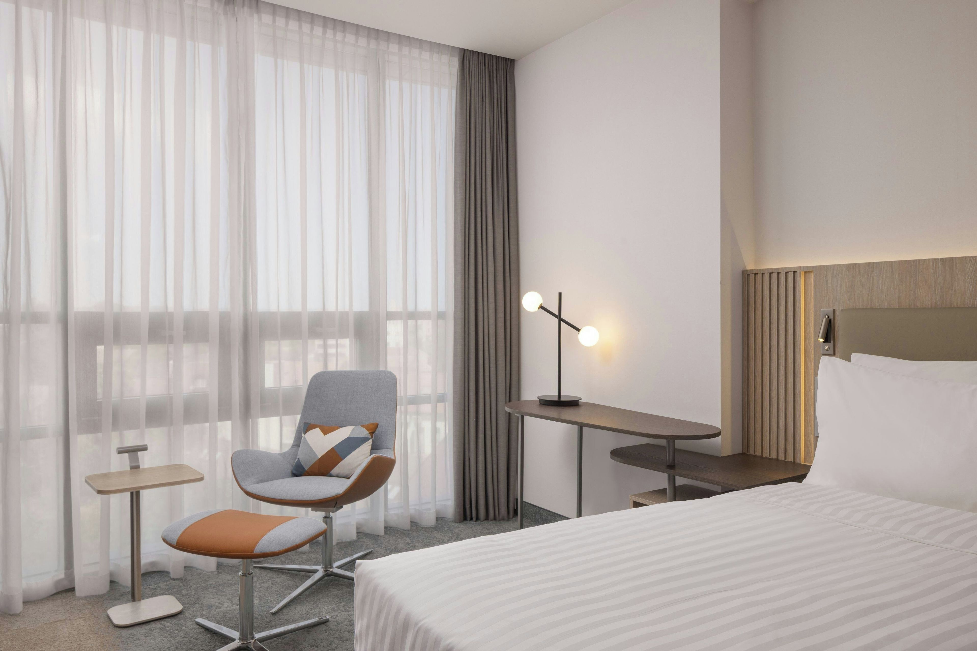 Una habitación de hotel con una cama, una silla, una mesita, un escritorio y una lámpara.