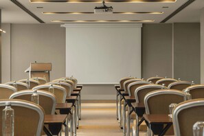 Un salón de conferencias con filas de sillas, un atril y una pantalla de proyección.