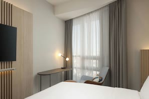 A hotel room with a bed, a TV mounted on the wall, a desk with a lamp, and a chair. - Courtyard by Marriott Downtown Sibiu (Sibiu)