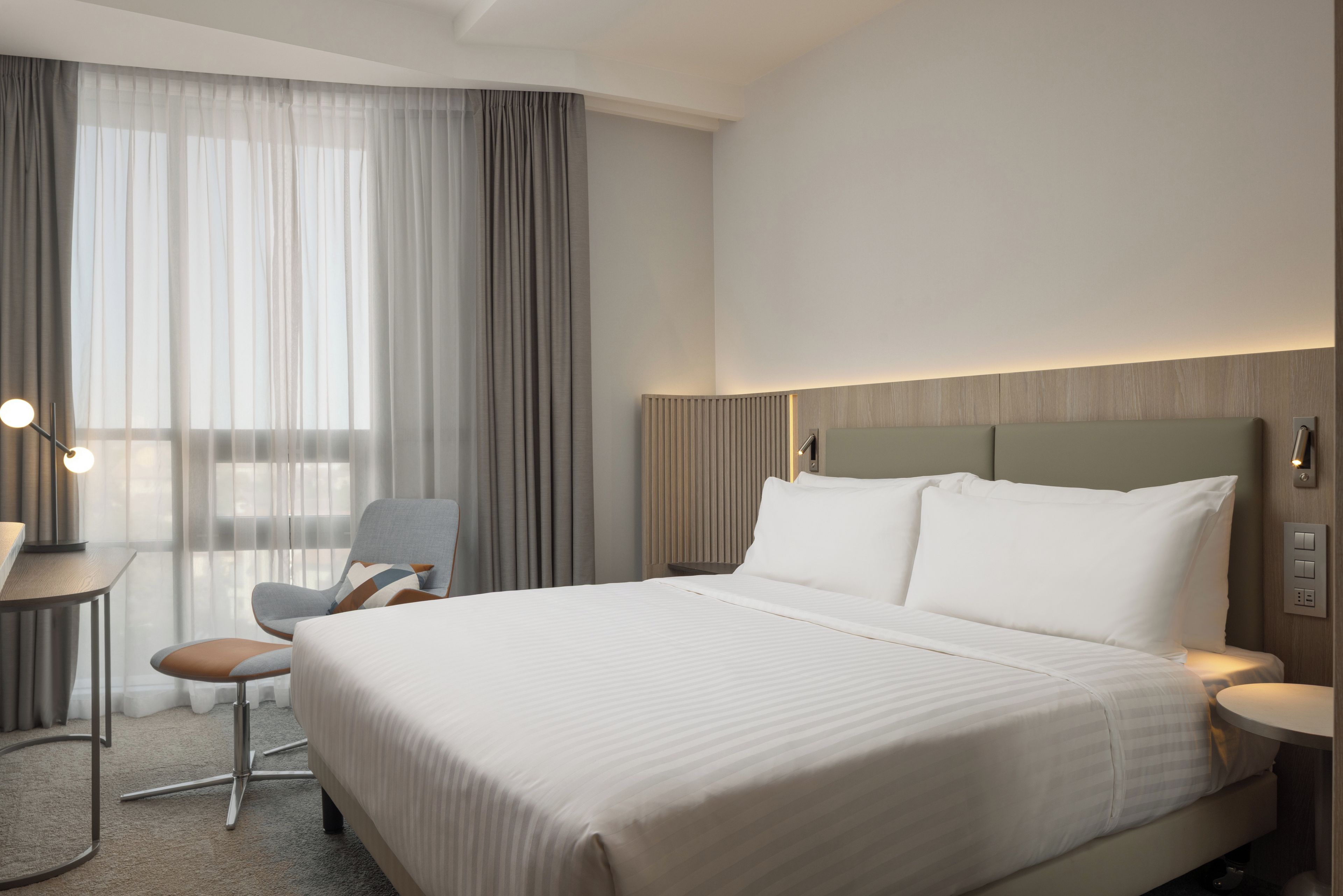 Una habitación de hotel con una cama grande, un escritorio, una silla y un ventanal con cortinas.