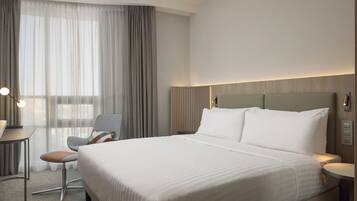 Una habitación de hotel con una cama grande, un escritorio, una silla y un ventanal con cortinas.