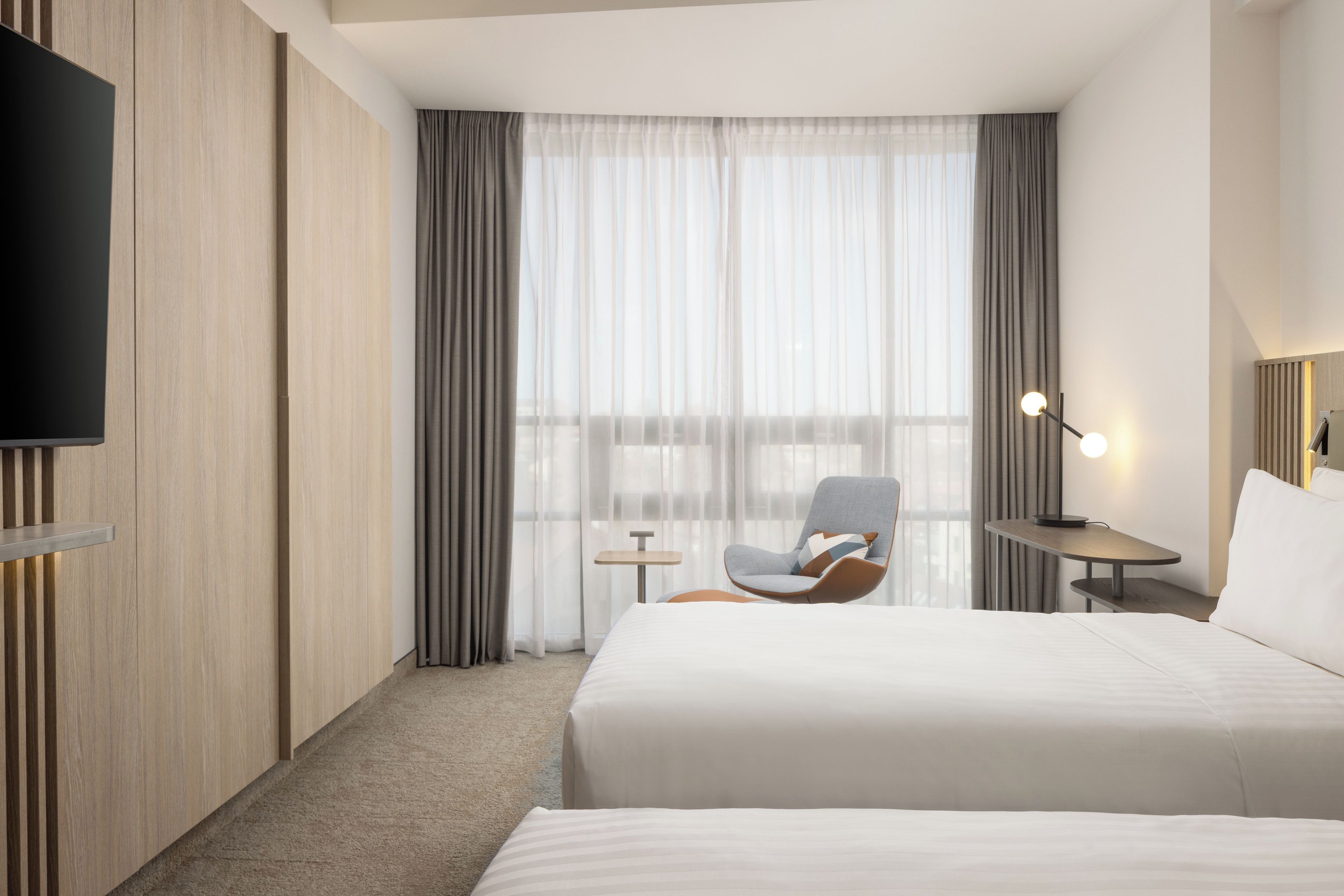 A hotel room with a bed, a chair, a desk, a TV, and a window with curtains.
