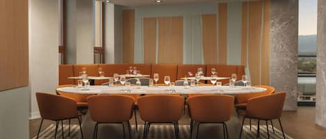 Un comedor moderno con una mesa redonda dispuesta para seis personas, rodeada de sillas naranjas, y vistas a la ciudad a través de un ventanal grande.