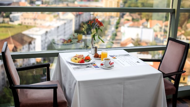 A dining table with a meal, a vase with flowers, and a city view through large windows. - Courtyard by Marriott Downtown Sibiu (Sibiu)