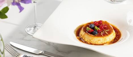 Un dessert servi sur une assiette carrée, un verre de vin blanc et une fourchette posée sur une table en marbre.