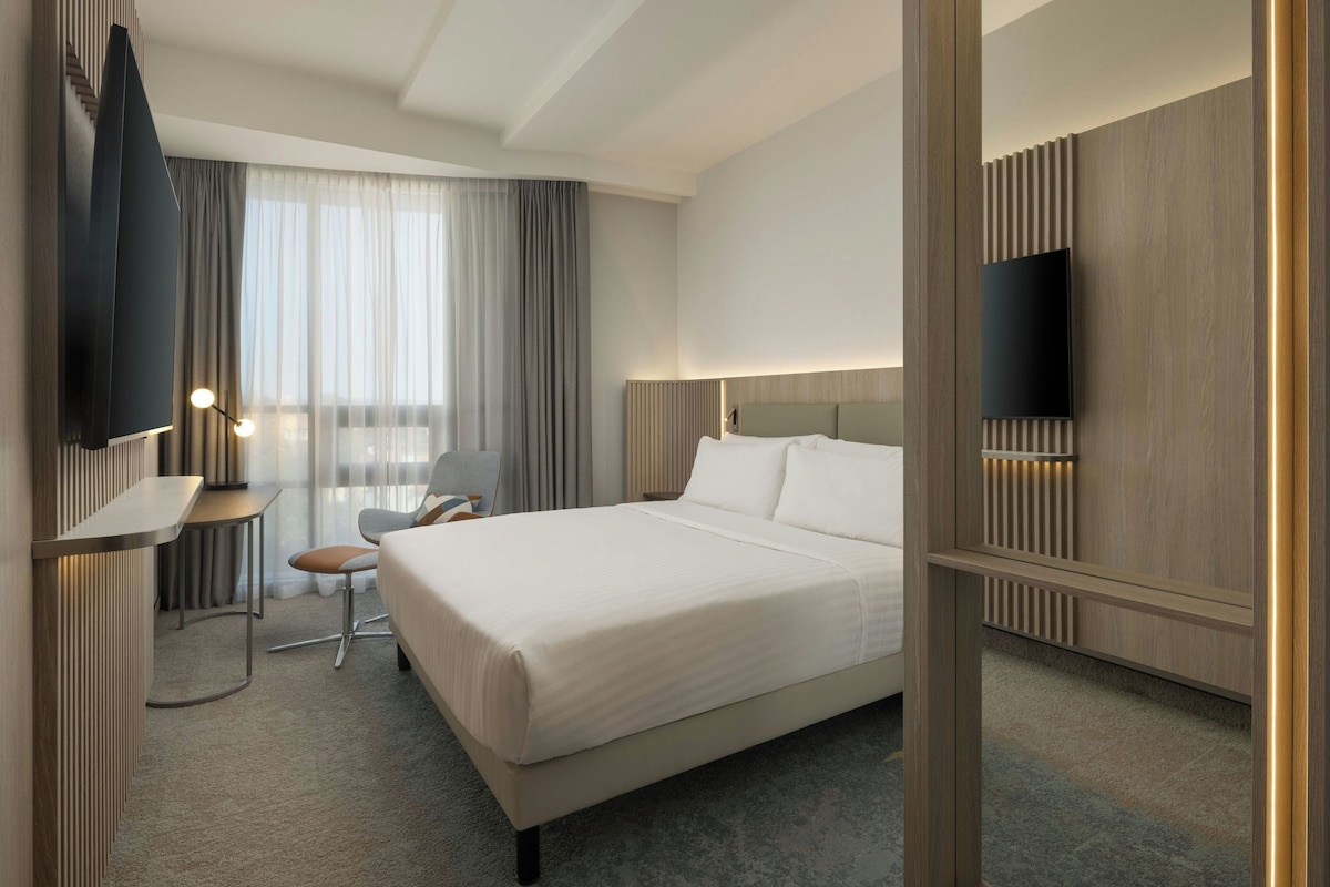 Een hotelkamer met een bed, een bureau, een stoel, een televisie en een raam met gordijnen.