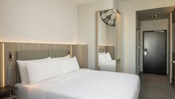 Una habitación de hotel con una cama grande, una mesita de noche, un espejo y una puerta.