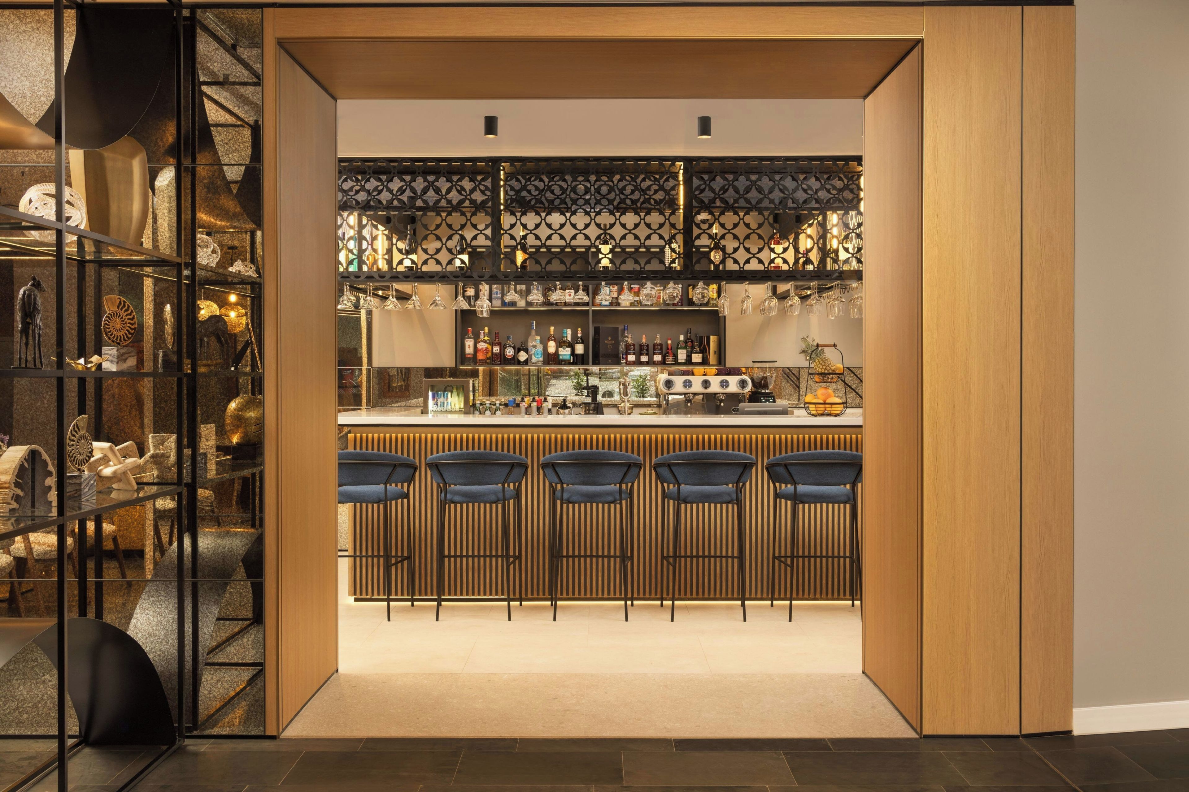 Zona de bar con barra, taburetes y una exhibición de botellas.