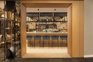A bar area with a counter, bar stools, and a display of bottles. - Courtyard by Marriott Downtown Sibiu (Sibiu)
