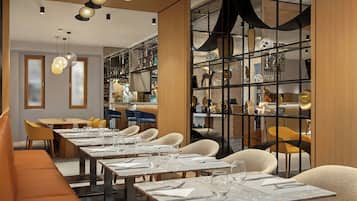 A modern dining area with multiple tables and chairs, a bar area with shelves of bottles, and a decorative wall with a geometric pattern.