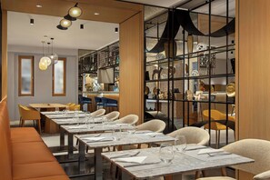 A modern dining area with multiple tables and chairs, a bar area with shelves of bottles, and a decorative wall with a geometric pattern. - Courtyard by Marriott Downtown Sibiu (Sibiu)