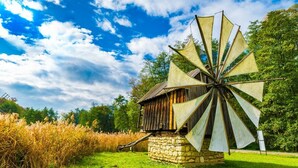 A windmill with a stone base and wooden structure, set in a grassy field with trees in the background. - Courtyard by Marriott Downtown Sibiu (Sibiu)