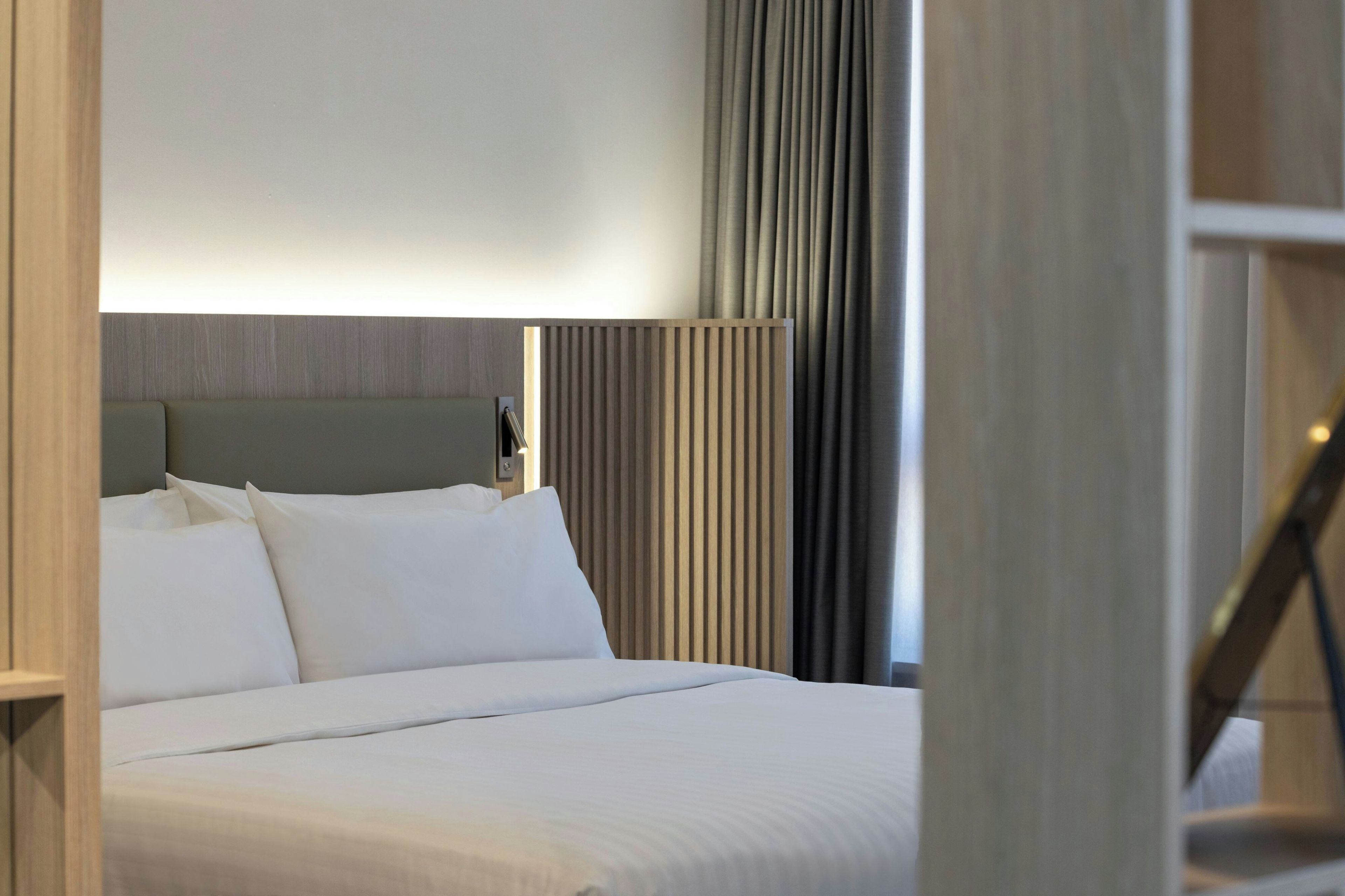 A hotel room with a bed, a headboard, a bedside table, and a window with curtains.