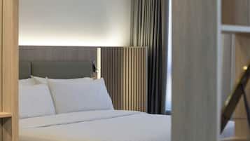 A hotel room with a bed, a headboard, a bedside table, and a window with curtains.