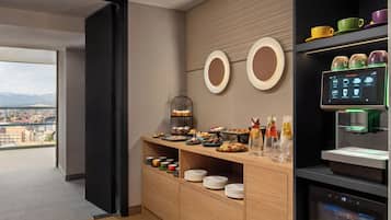 A modern hotel room with a breakfast bar, a coffee machine, and a view of the city.