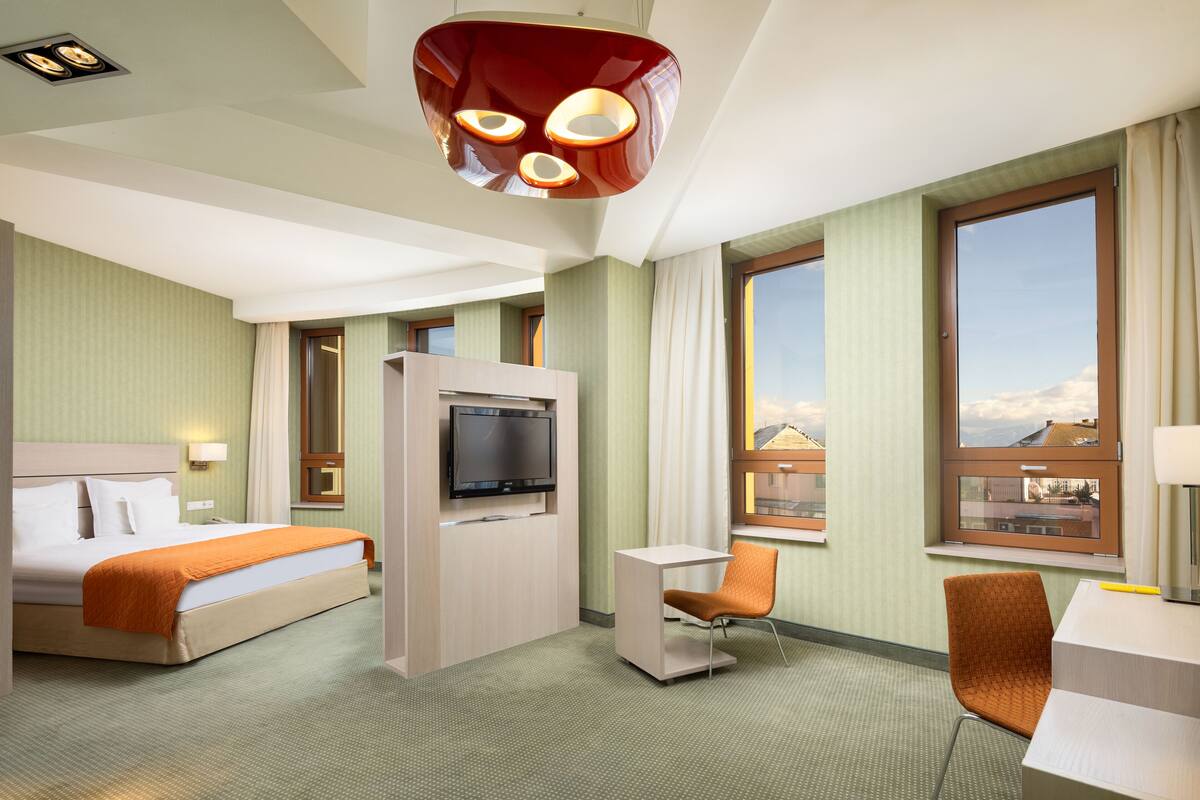 A hotel room with a bed, a TV, a desk, and a chair.