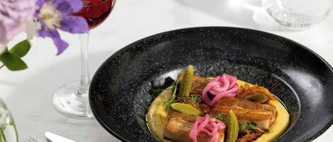 A black plate with food, a glass of red wine, and a fork on a table.