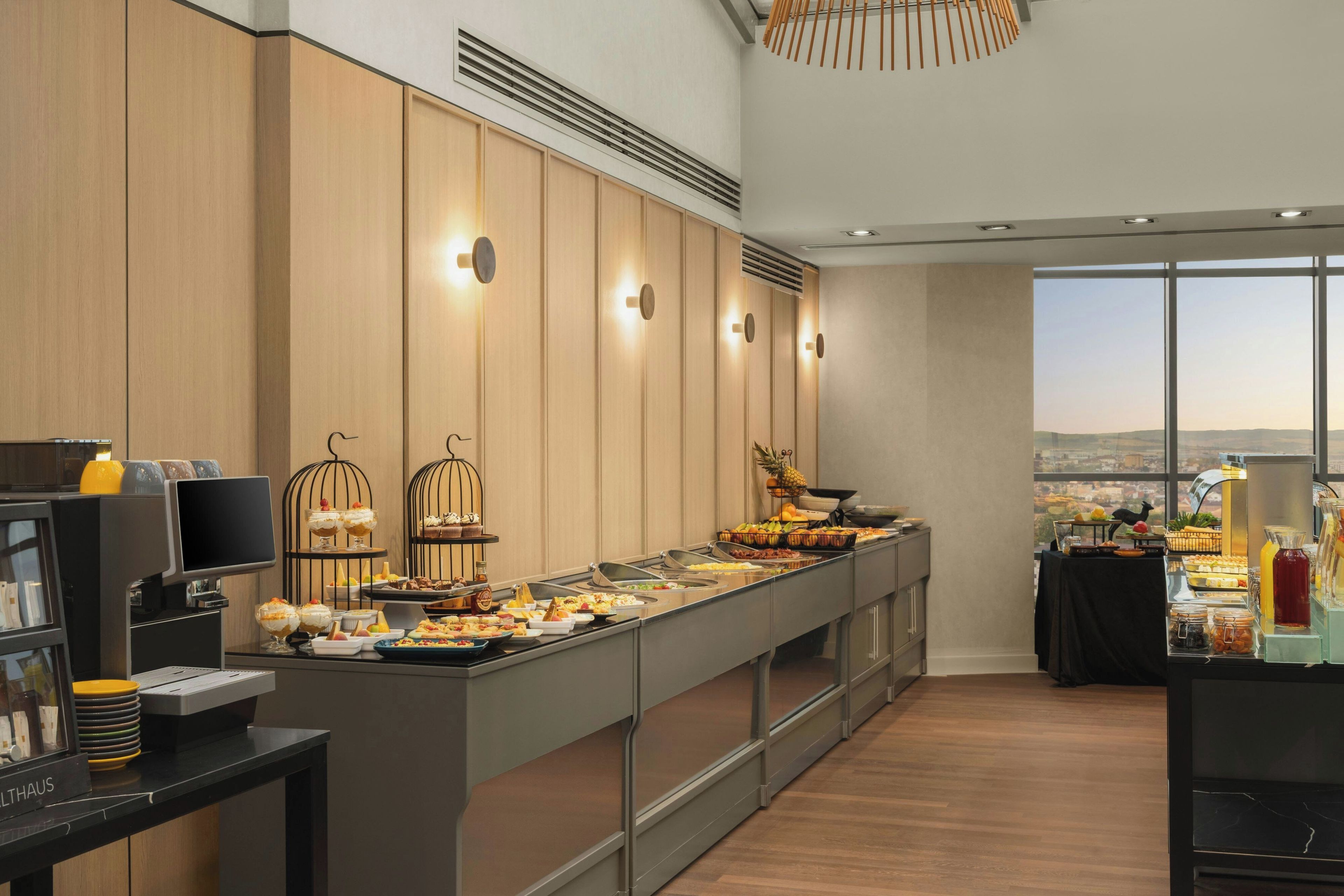 A buffet setup with a variety of food items and a view of the city through large windows.