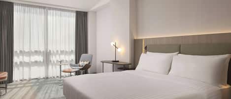 Una habitación de hotel con una cama grande, una silla, una mesita y una lámpara.