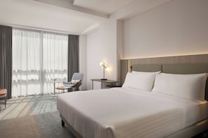 A hotel room with a large bed, a chair, a small table, and a lamp. - Courtyard by Marriott Downtown Sibiu (Sibiu)